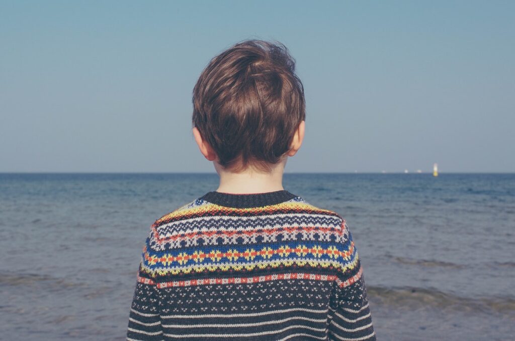 child wearing a sweater looking out at the ocean