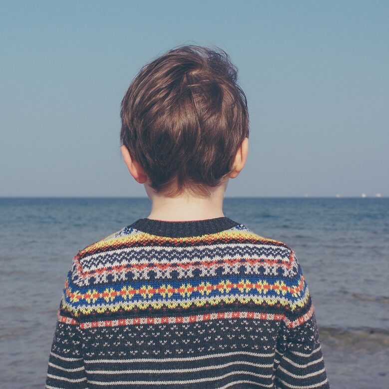 child wearing a sweater looking out at the ocean